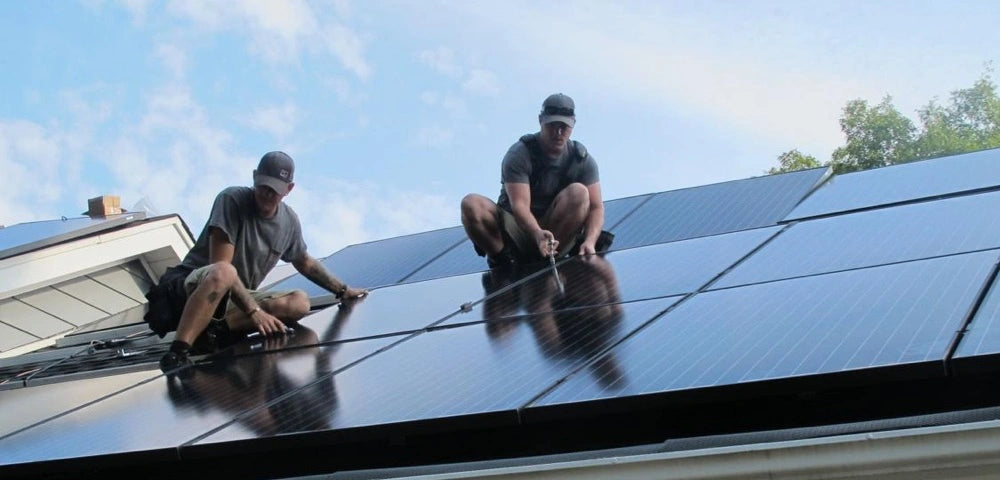 Deux installateurs de toiture solaire en train de fixer un panneau photovoltaïque sur une maison